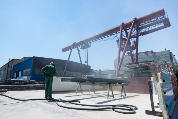 factory for cleaning of metal by sandblasting. a worker cleans the metal by sandblasting